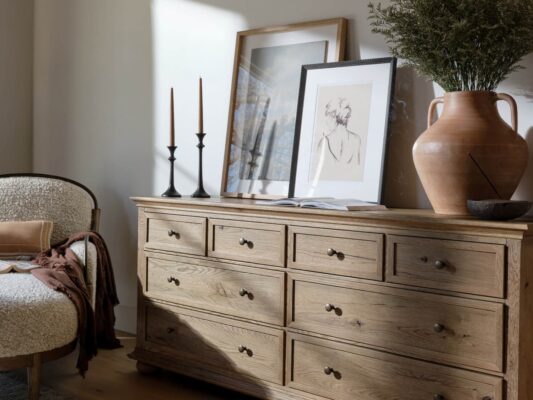 Wooden dresser with art and decor in sunlit room.