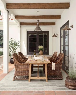 Cozy outdoor dining area with wicker chairs and wooden beams. All centered by a beautiful outdoor rug from Amber Lewis x Loloi